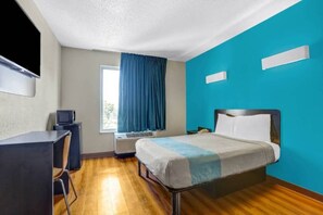 Quarto de hotel com cama, escrivaninha e televisão.