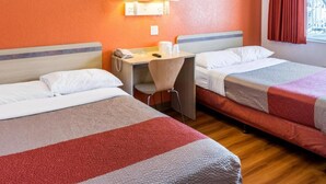 Quarto de hotel com duas camas, uma escrivaninha com cadeira, telefone e janela com cortinas.
