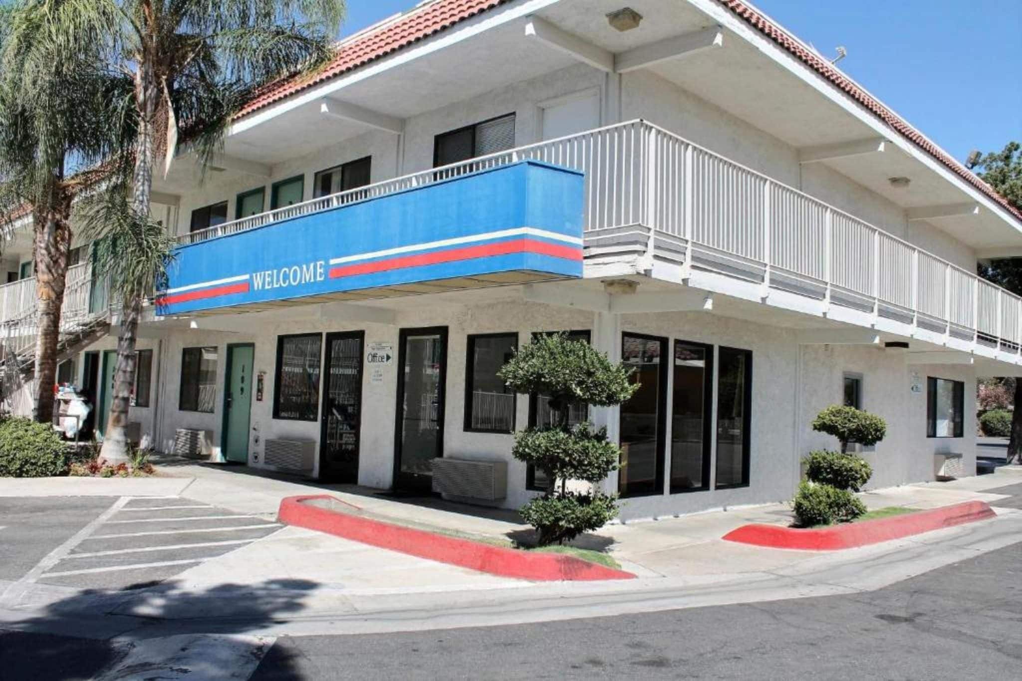 Edifício de dois andares com uma placa de 'WELCOME', entrada coberta e estacionamento.