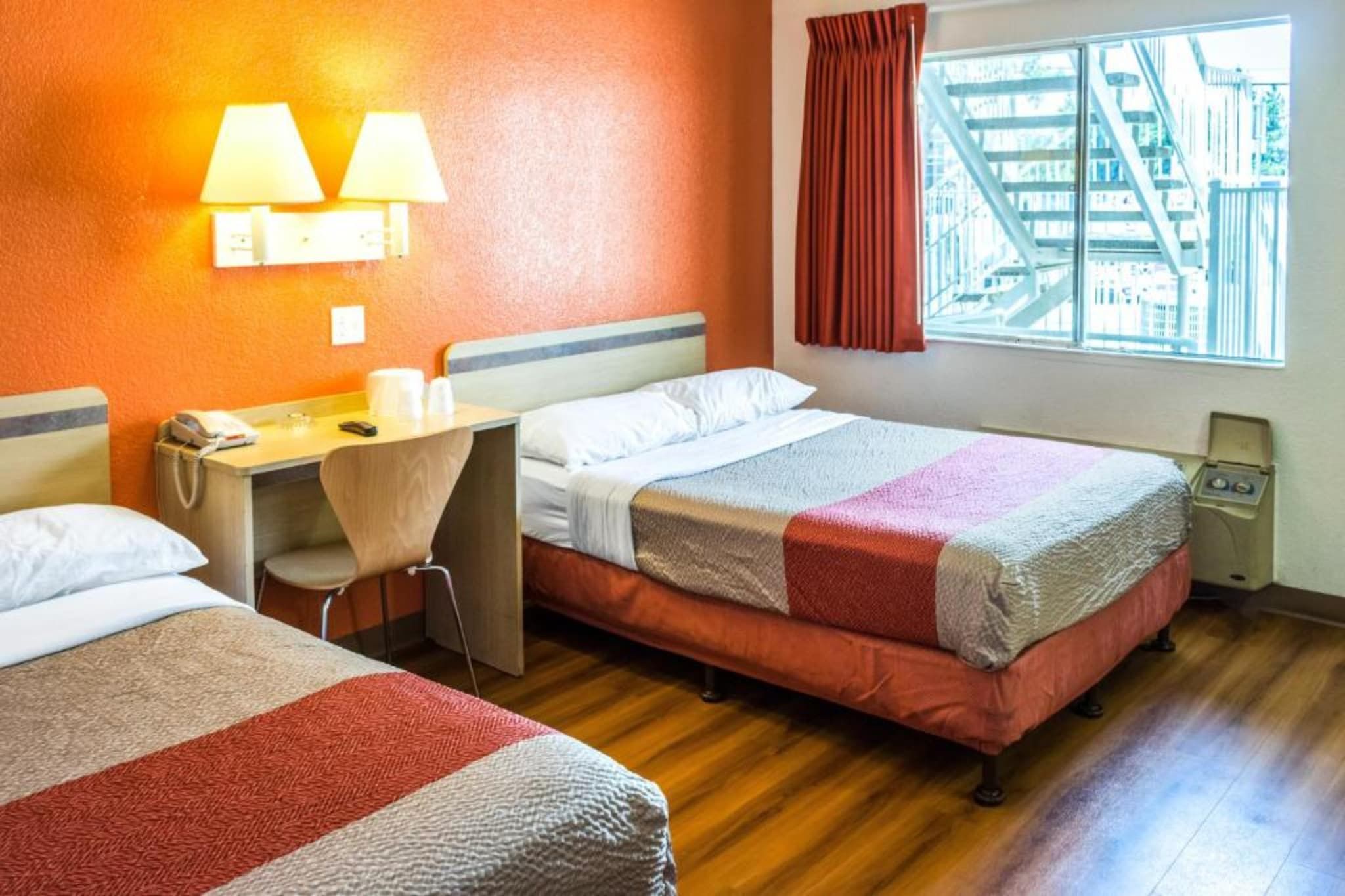 Quarto de hotel com duas camas, uma mesa, uma cadeira, um telefone e janela com vista para edifícios.