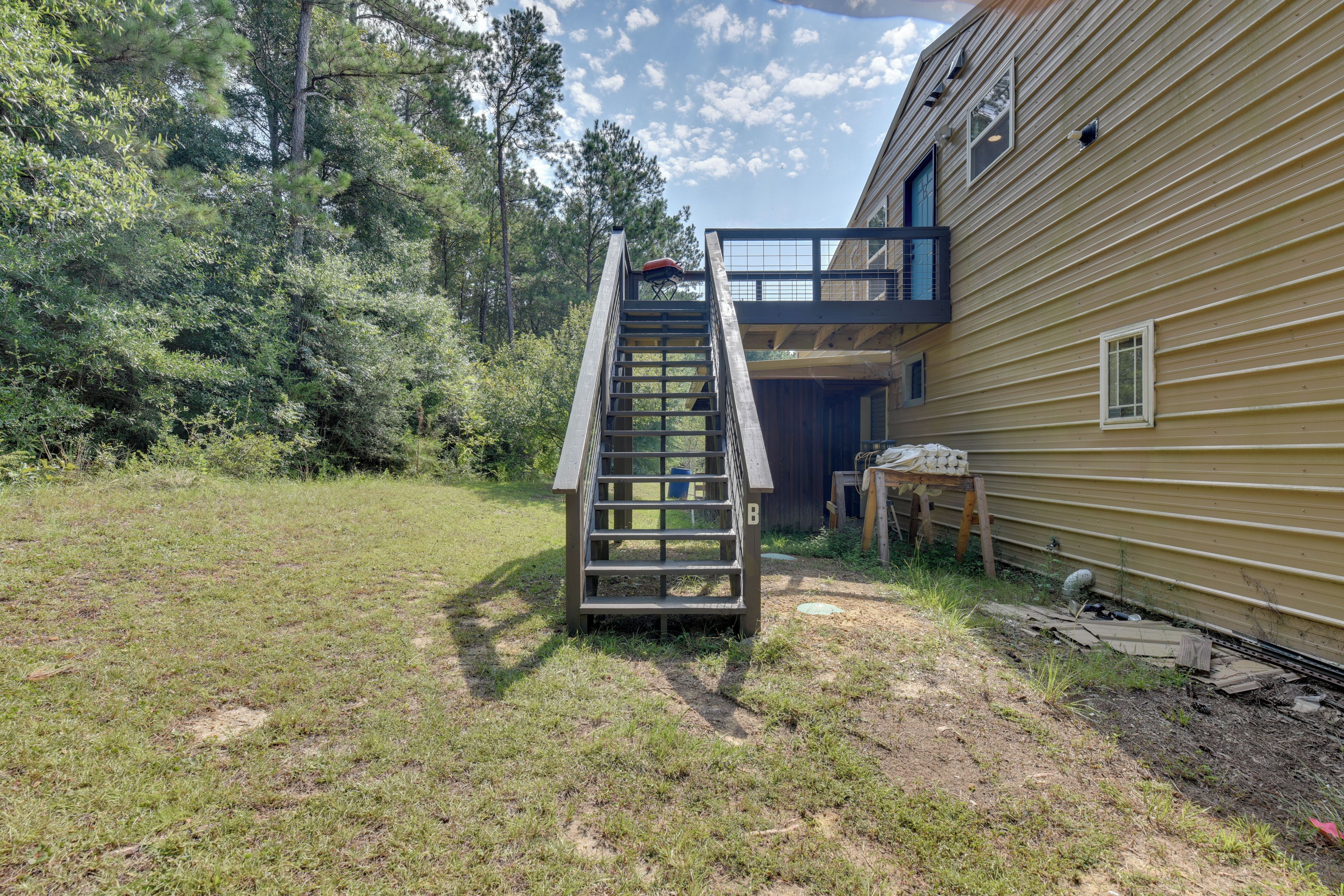 Una escalera de madera que conduce a una terraza con vista a una casa y árboles circundantes.