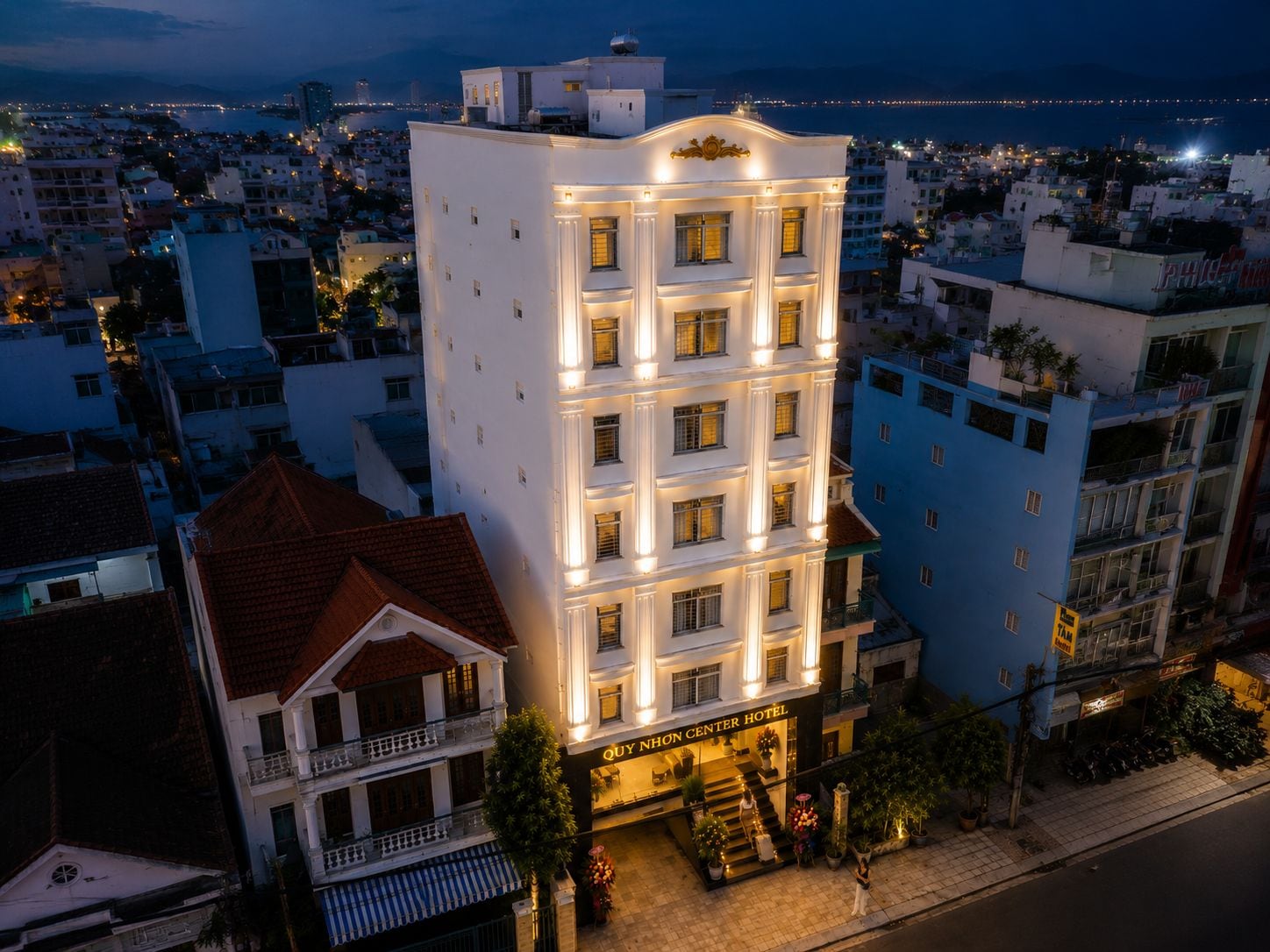 Un hotel de varios pisos con entrada central, balcones y vistas del paisaje urbano circundante.