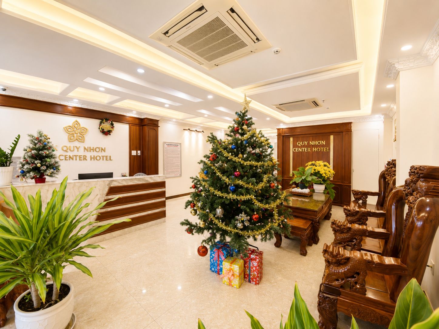 Zona de recepción de un hotel con un árbol de Navidad, una mesa de recepción y un cartel que dice 'QUY NHON CENTER HOTEL'.