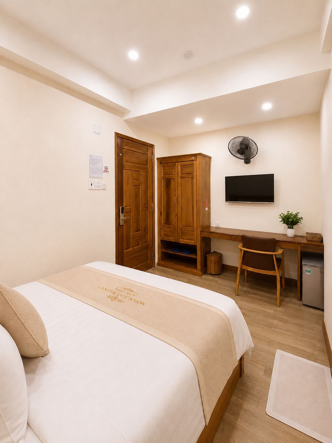 Quarto de hotel com cama, escrivaninha, cadeira, televisão e uma pequena cozinha.