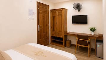 Quarto de hotel com cama, escrivaninha, cadeira, televisão e uma pequena cozinha.