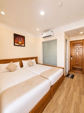A hotel room with two beds, a wooden headboard, a painting on the wall, an air conditioning unit, and a wooden door.