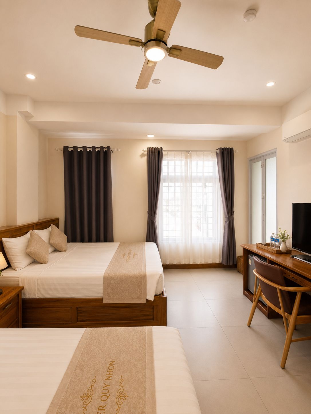 A hotel room with a bed, a desk, a chair, a ceiling fan, and a window with curtains.