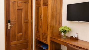 Quarto com guarda-roupa de madeira, escrivaninha com cadeira, televisão e ventoinha fixada na parede.