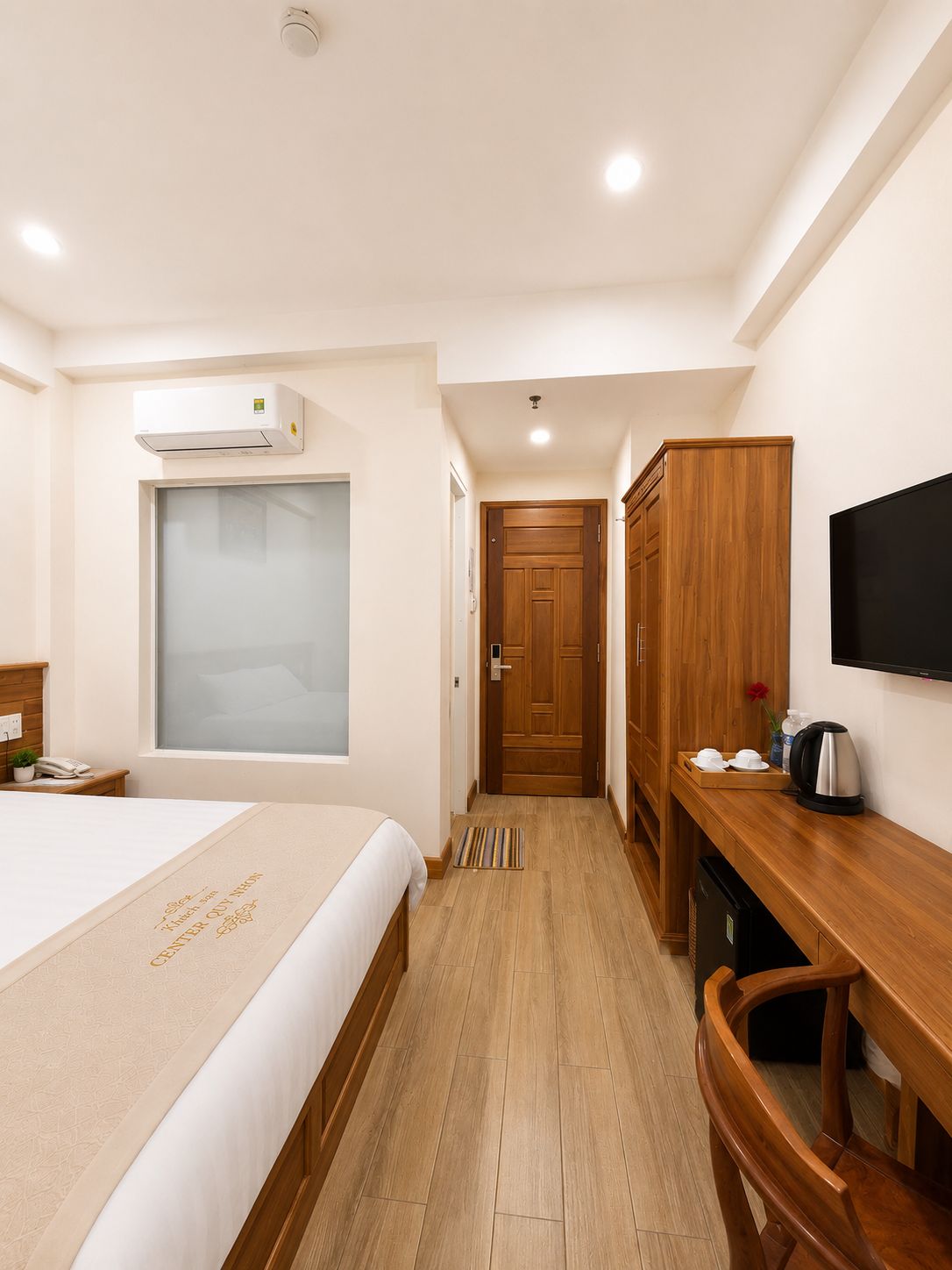 Quarto de hotel com uma cama, uma escrivaninha, uma televisão e um guarda-roupa.