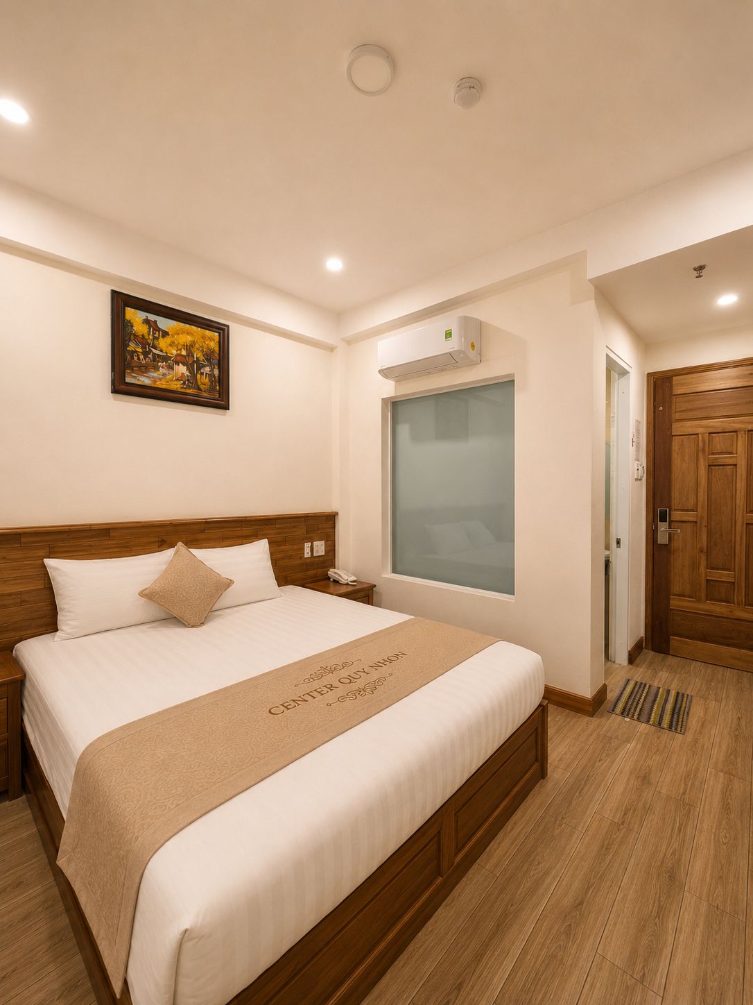 Una camera d'albergo con un letto, un quadro appeso al muro, un condizionatore d'aria e una porta in legno.