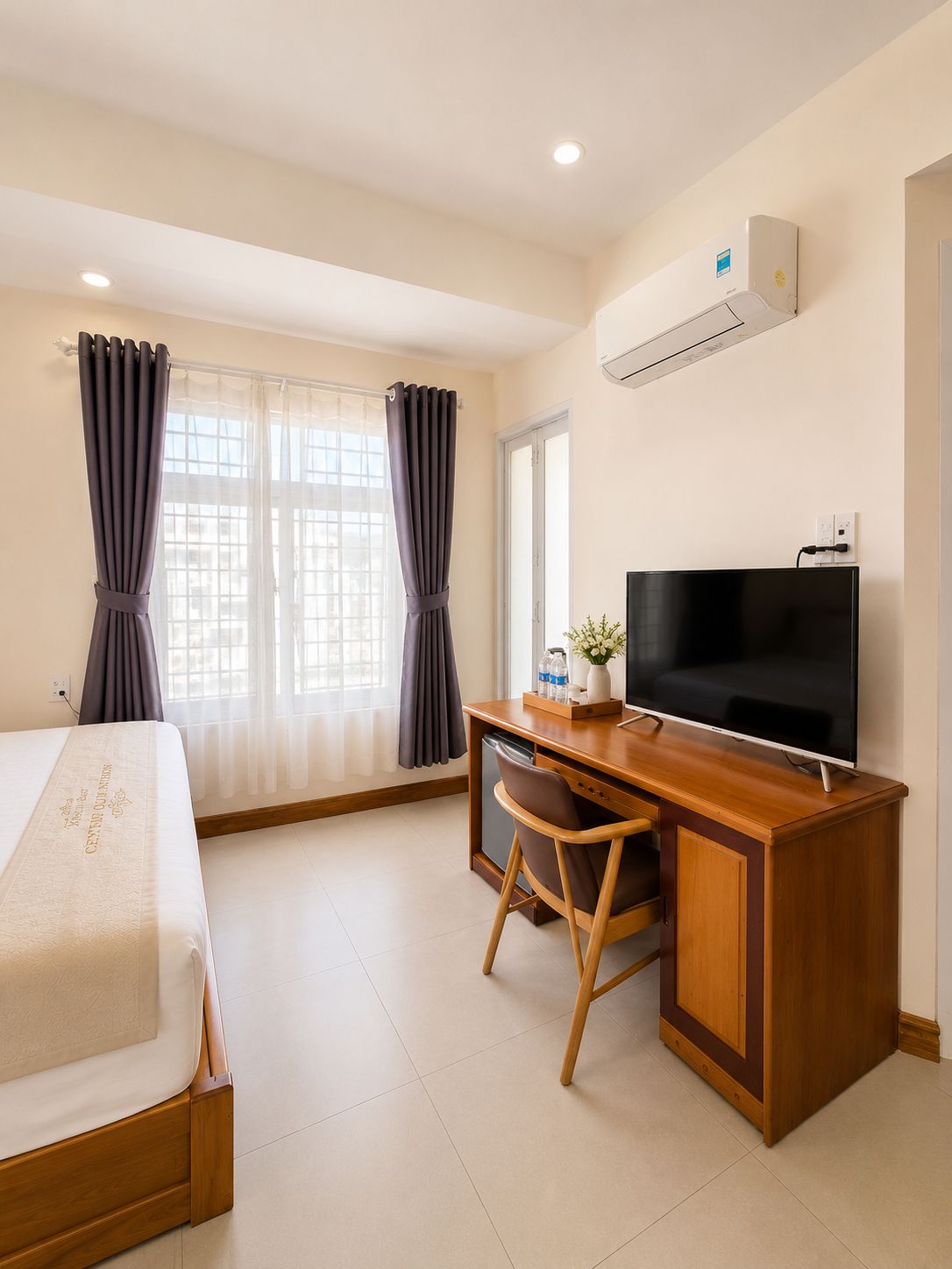 A hotel room with a bed, a desk with a television, and a window with curtains.