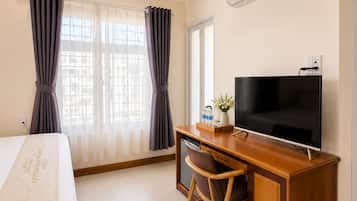 Habitación de hotel con cama, escritorio con televisor y ventana con cortinas.