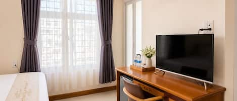 Habitación de hotel con cama, escritorio con televisor y ventana con cortinas.