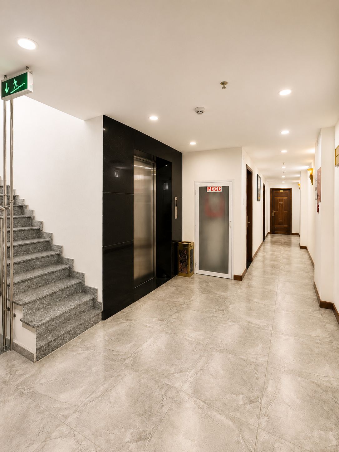 Um corredor de hotel com uma escada, um elevador e uma porta identificada com 'PCCC'.
