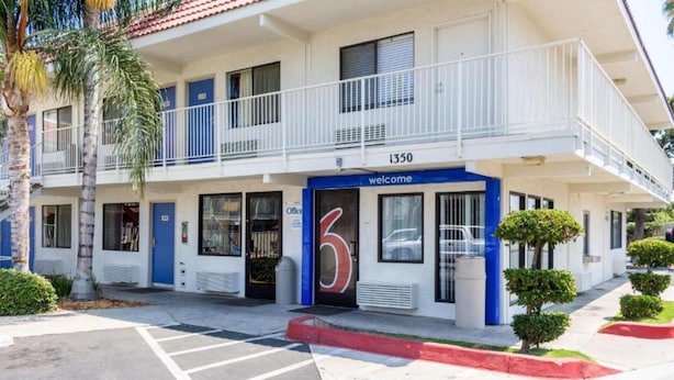 Un motel à deux étages, avec un panneau indiquant le chiffre « 6 », un balcon et une enseigne « Bienvenue ».