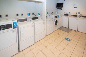 Een wasserette met meerdere wasmachines en drogers, een betegelde vloer en een aan de muur bevestigde televisie.