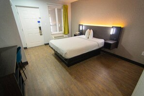 A hotel room with a bed, bedside table, and a desk with a chair.