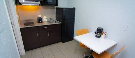 A compact kitchen with dark cabinets, a microwave, a refrigerator, a coffee maker, and a small dining table with two chairs.