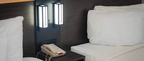 A hotel room with two beds, a bedside table with a telephone, and wall-mounted lighting.