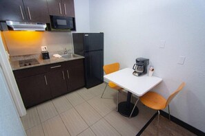 Una cocina compacta con microondas, refrigerador, lavamanos y una pequeña mesa de comedor con sillas.