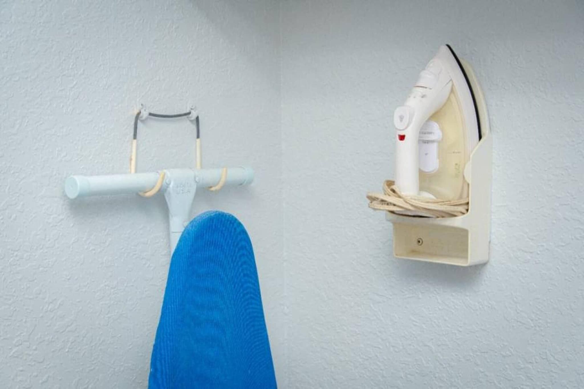 Un rincón de una habitación con una pared blanca, una silla azul y un centro de planchado fijado a la pared.
