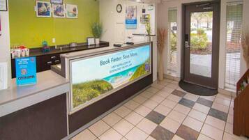 A reception area with a digital screen displaying a booking message, a counter with a sign for members, and a tiled floor.