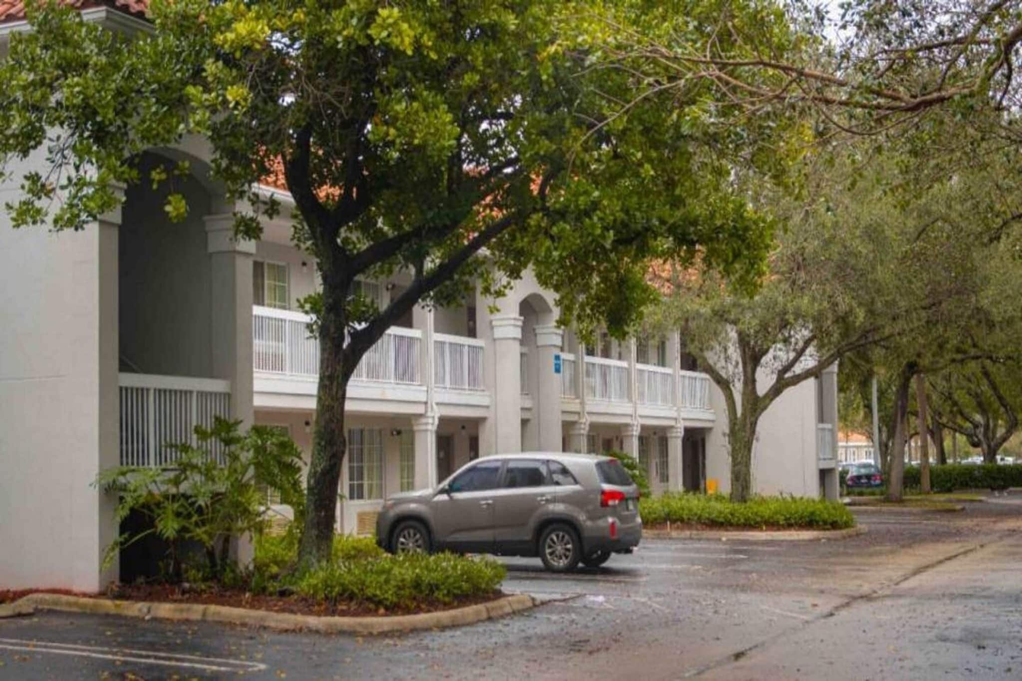 A building with a car parked in front, surrounded by trees and greenery.