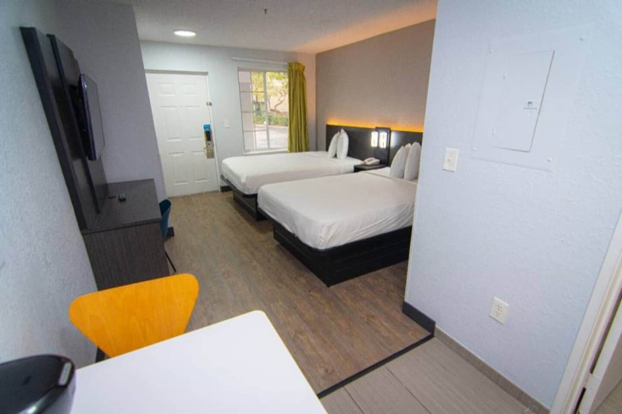 A hotel room with two beds, a desk, a chair, and a television.