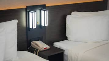 A hotel room with two beds, a bedside table with a telephone, and wall-mounted lighting.