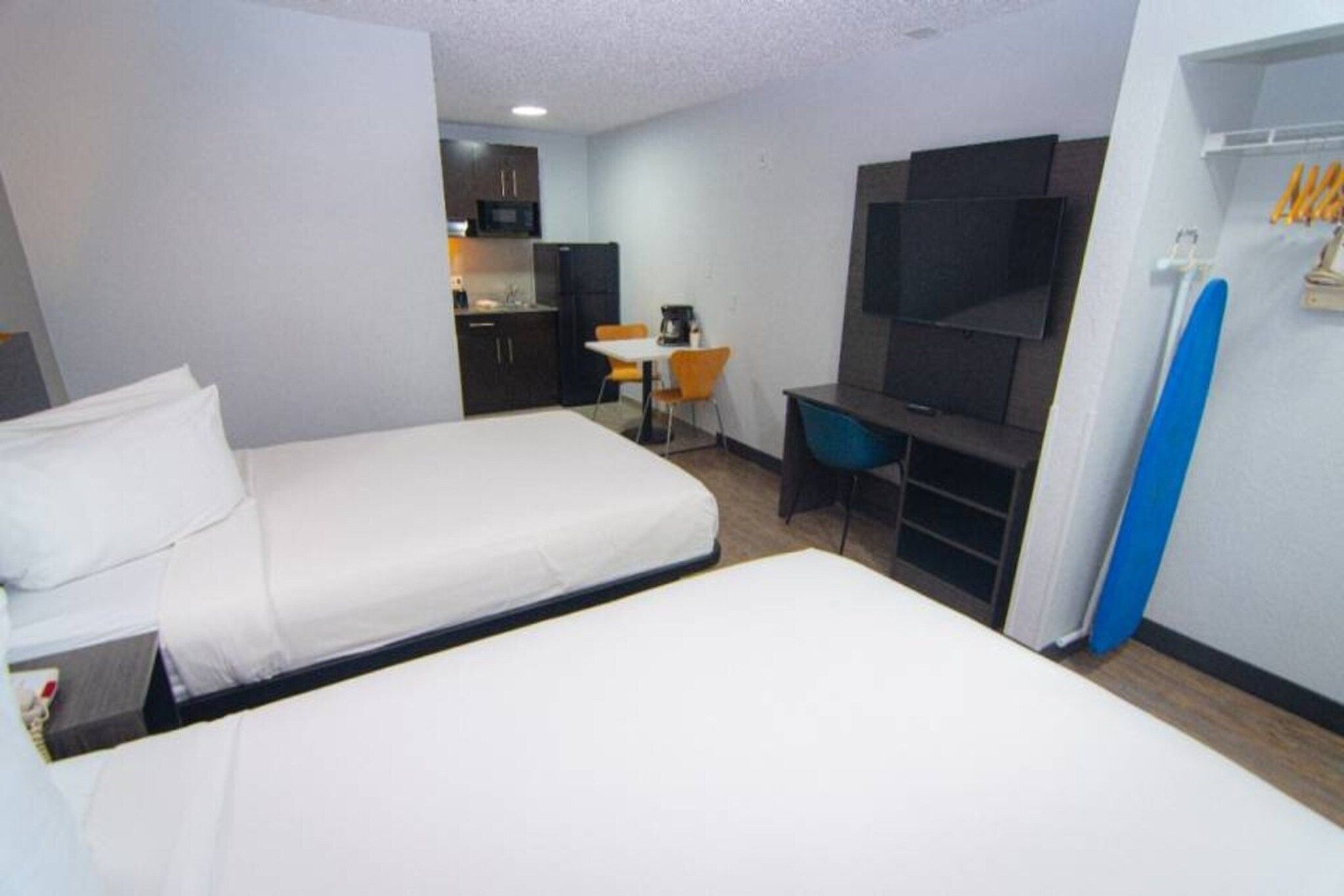 Une chambre d’hôtel avec deux lits, un bureau, une chaise, un téléviseur et, au fond, une petite cuisine.