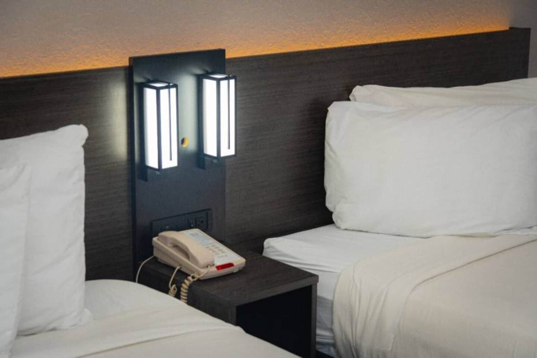 Habitación de hotel con dos camas, una mesita de noche con teléfono e iluminación en la pared.