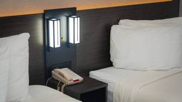 Habitación de hotel con dos camas, una mesita de noche con teléfono e iluminación en la pared.