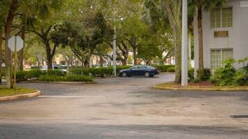 A residential street with a parked car, trees, and a building with a white facade.