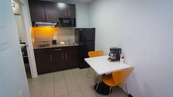 Una cocina compacta con armarios oscuros, un refrigerador negro, una encimera blanca y una pequeña mesa con cafetera.