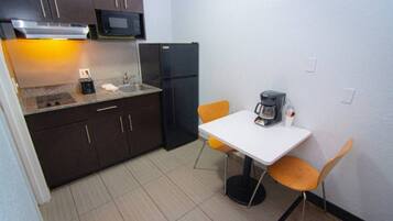 A compact kitchen with dark cabinets, a microwave, a refrigerator, a sink, and a small dining table with two chairs.