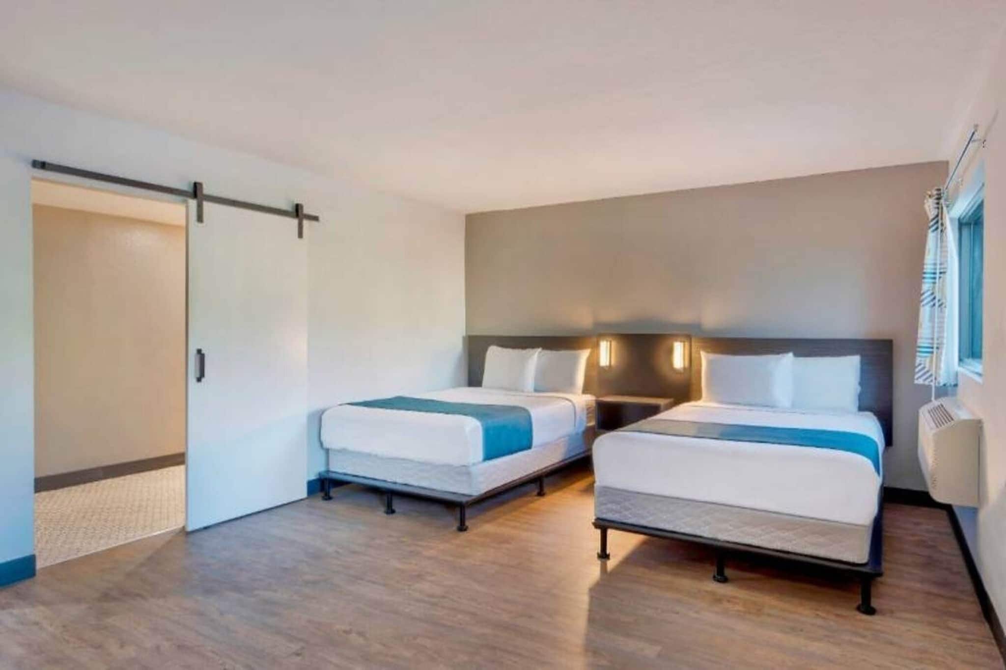Een hotelkamer met twee bedden, een schuifdeur en een groot raam met gordijnen.