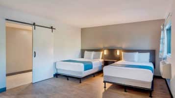 Een hotelkamer met twee bedden, een schuifdeur en een groot raam met gordijnen.