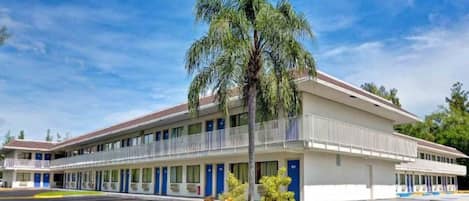 A motel with a two-story structure, a covered parking area, and a palm tree in front.