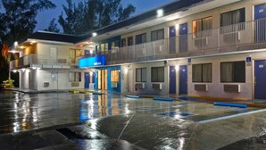Un motel a più piani con un ingresso blu, camere individuali con porte e un parcheggio.