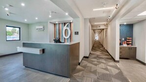 Un'area di reception di un hotel con una scrivania, un corridoio con tappeto decorato e vista all'esterno attraverso una finestra.