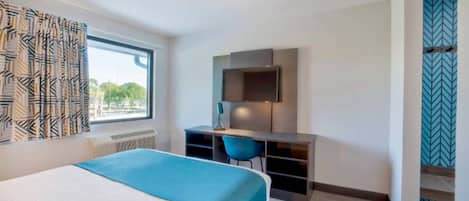 A hotel room with a bed, a desk, a chair, and a TV.