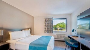 Una camera d'albergo con un letto, una scrivania, una sedia e una finestra vista alberi.