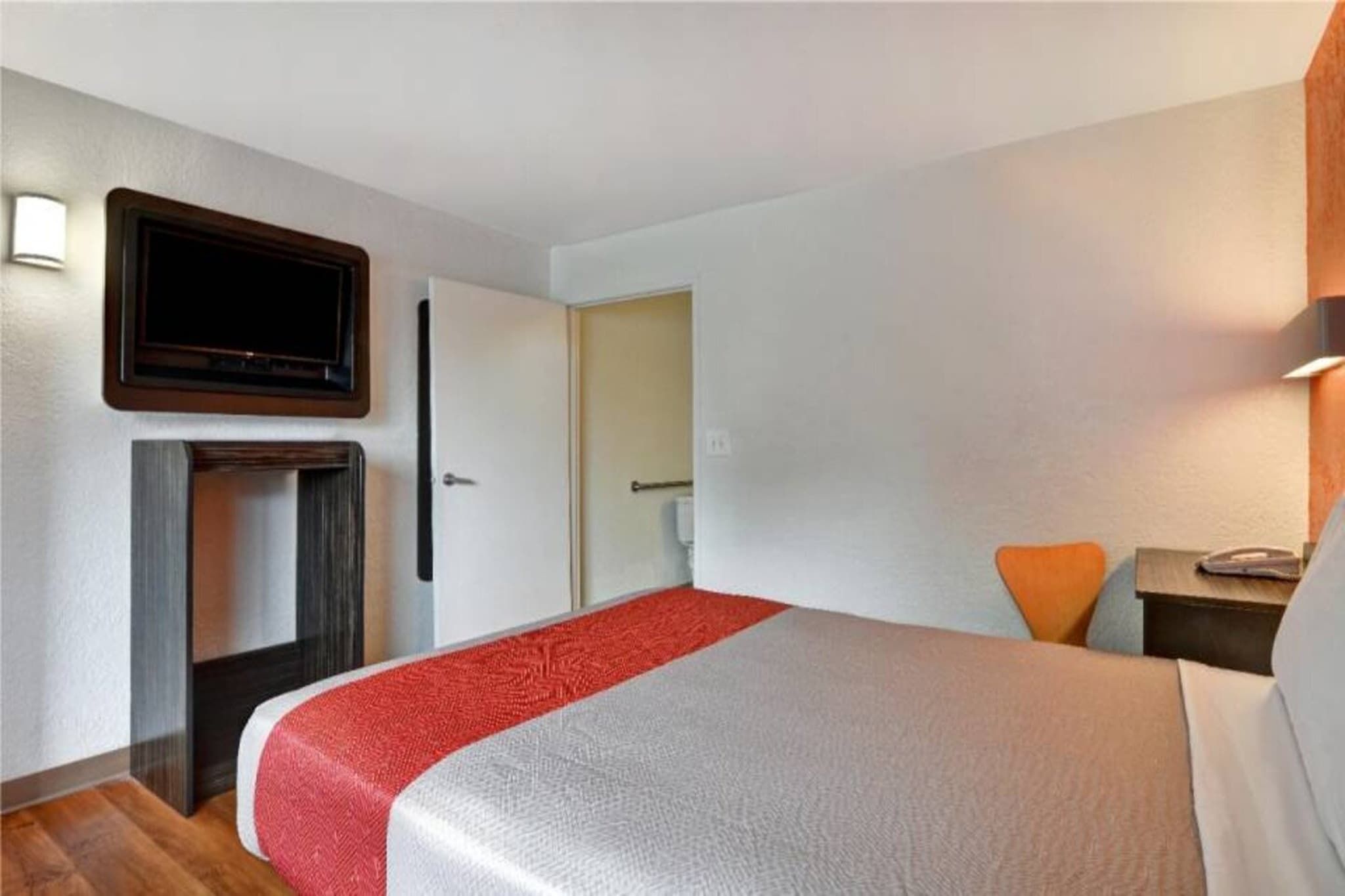 Habitación de hotel con cama, televisión montada en la pared, escritorio con silla y puerta que da a otra habitación.