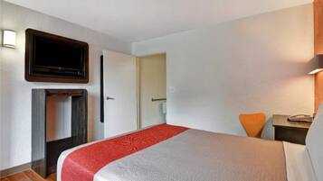 Habitación de hotel con cama, televisión montada en la pared, escritorio con silla y puerta que da a otra habitación.