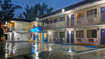Un motel de varios pisos con entrada central, habitaciones individuales en cada planta y aparcamiento.