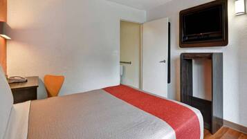 Habitación de hotel con cama, televisor montado en la pared y suelo de madera.