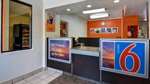 Zona de recepción de un hotel con un mostrador, un reloj y un cartel que indica el nombre del hotel, '6 Motel'.