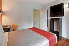 Habitació d'hotel amb un llit, una televisió penjada a la paret i un sòl de fusta.