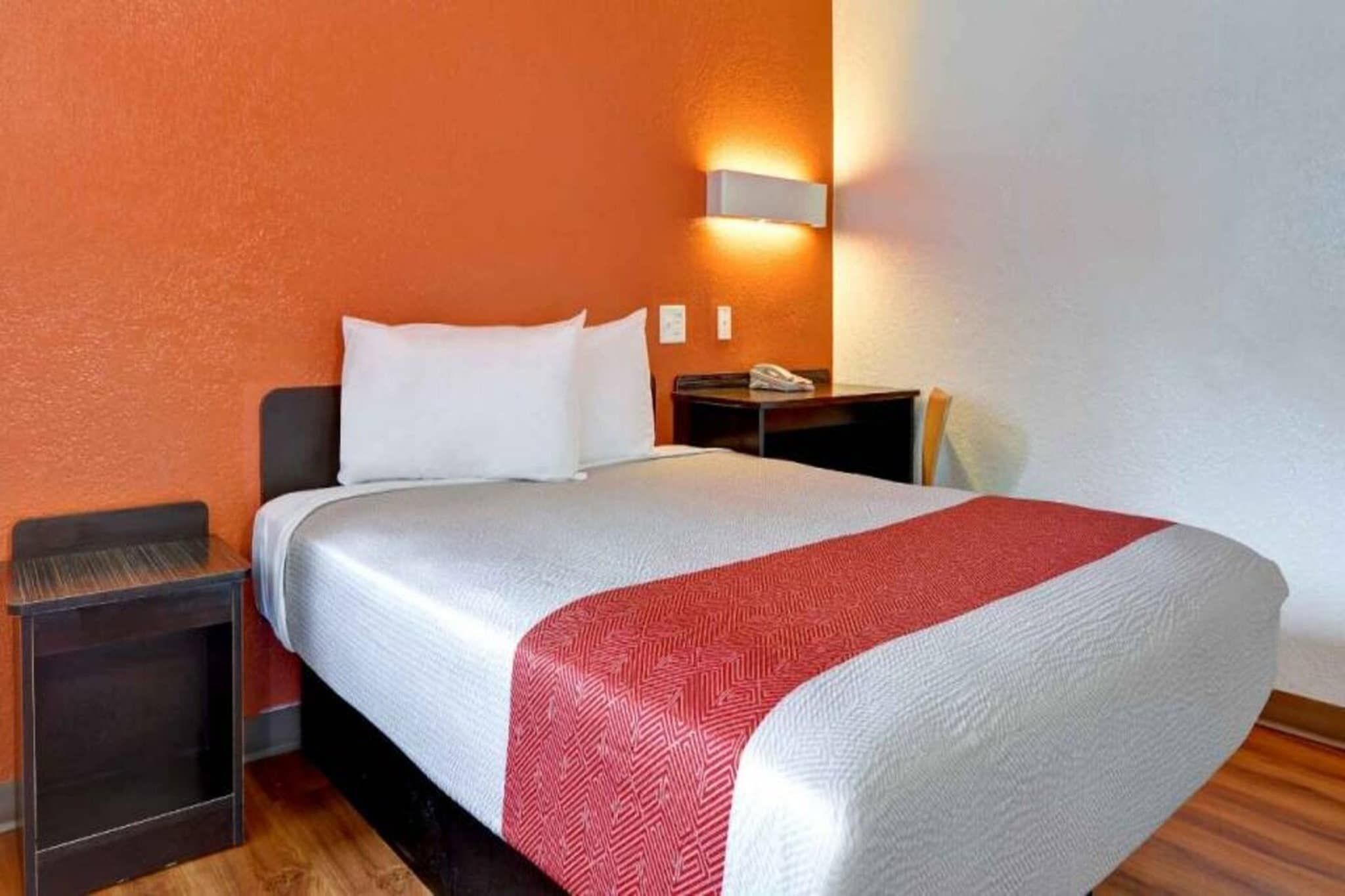 Habitación de hotel con cama, mesita de noche, teléfono e iluminación en la pared.