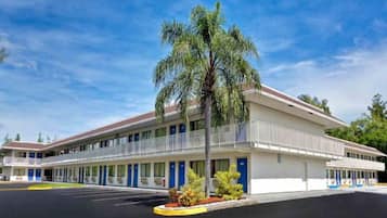 Un motel de dos pisos, con zona de estacionamiento techada y una palmera frente a él.